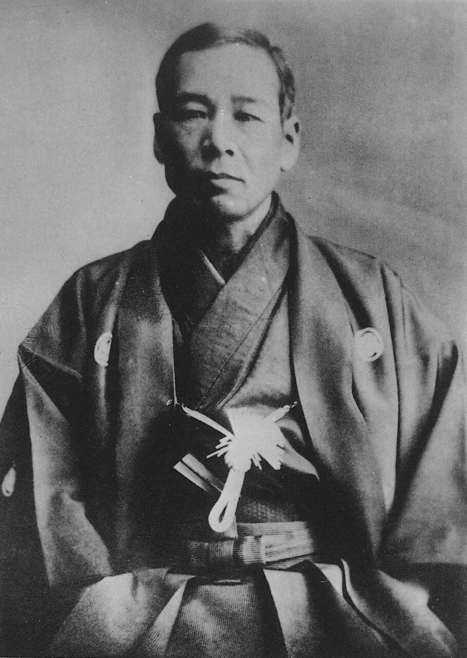 Crno-beli portret mu&scaron;karca u tradicionalnoj japanskoj odeći, snimljenog kako sedi i gleda pravo u kameru.