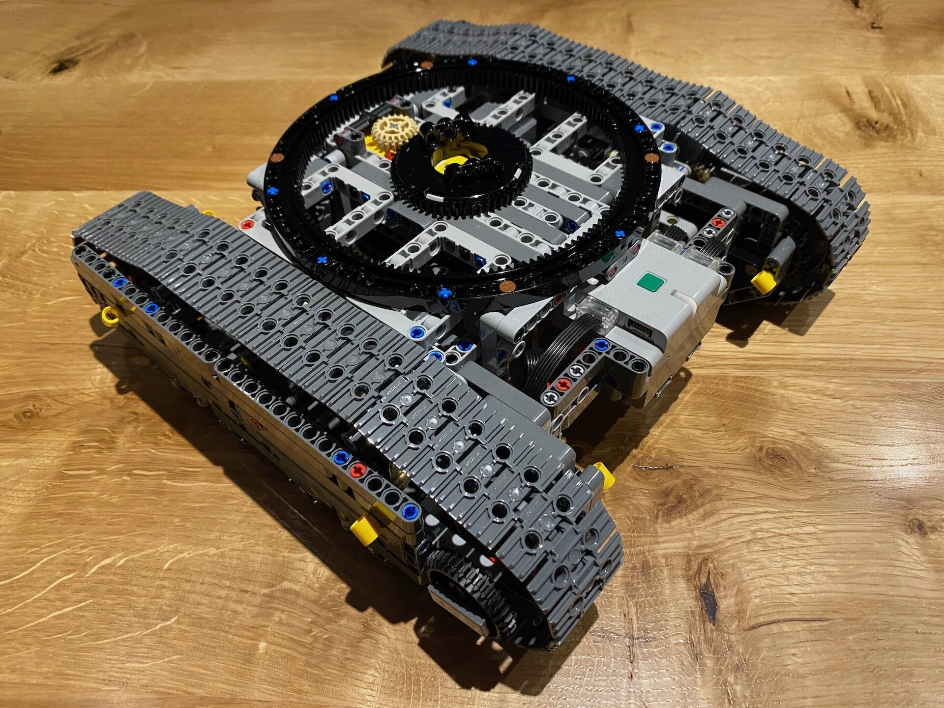 Delimično sastavljena gusenična šasija Lego Technic bagera na drvenom podu.