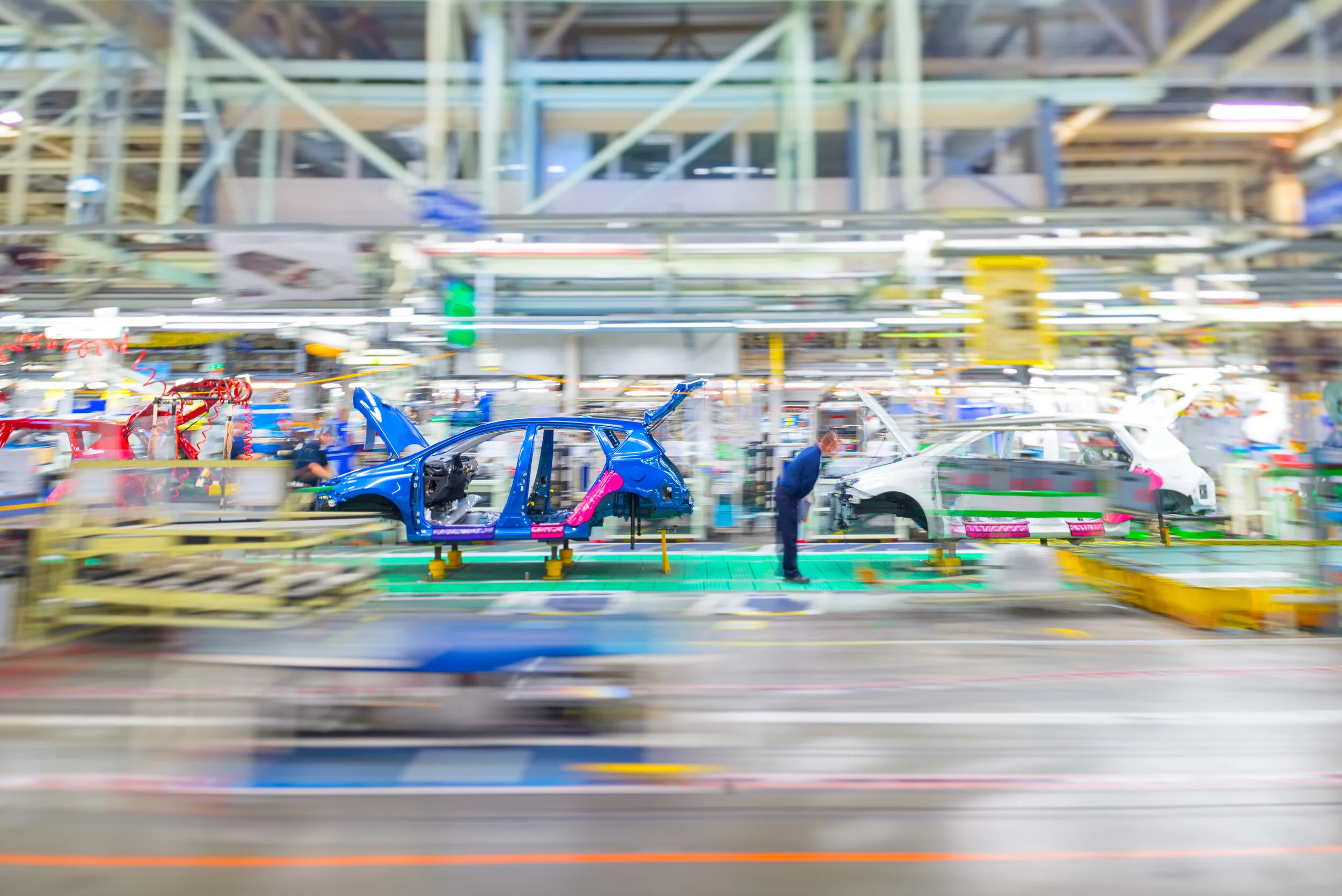 Zamućena fotografija fabričke trake sa nedovr&scaron;enim plavim i belim automobilima.