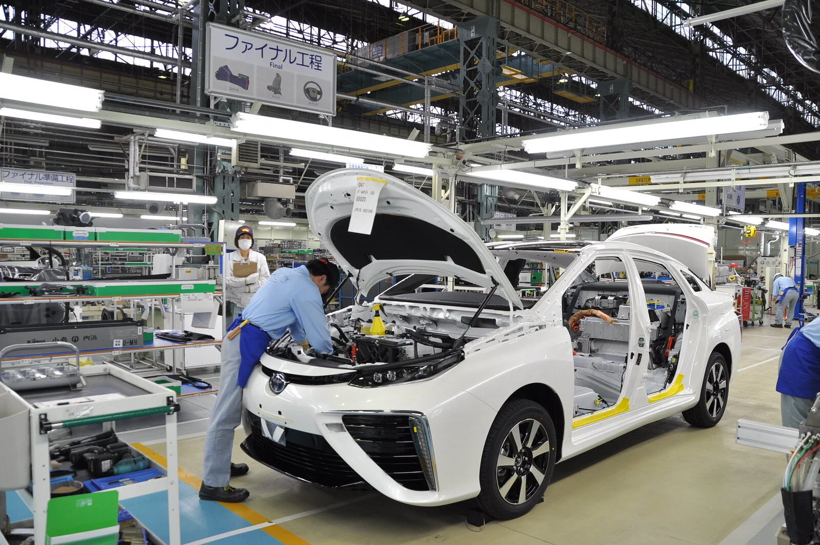 Radnik sklapa beli automobil u velikom fabričkom pogonu.