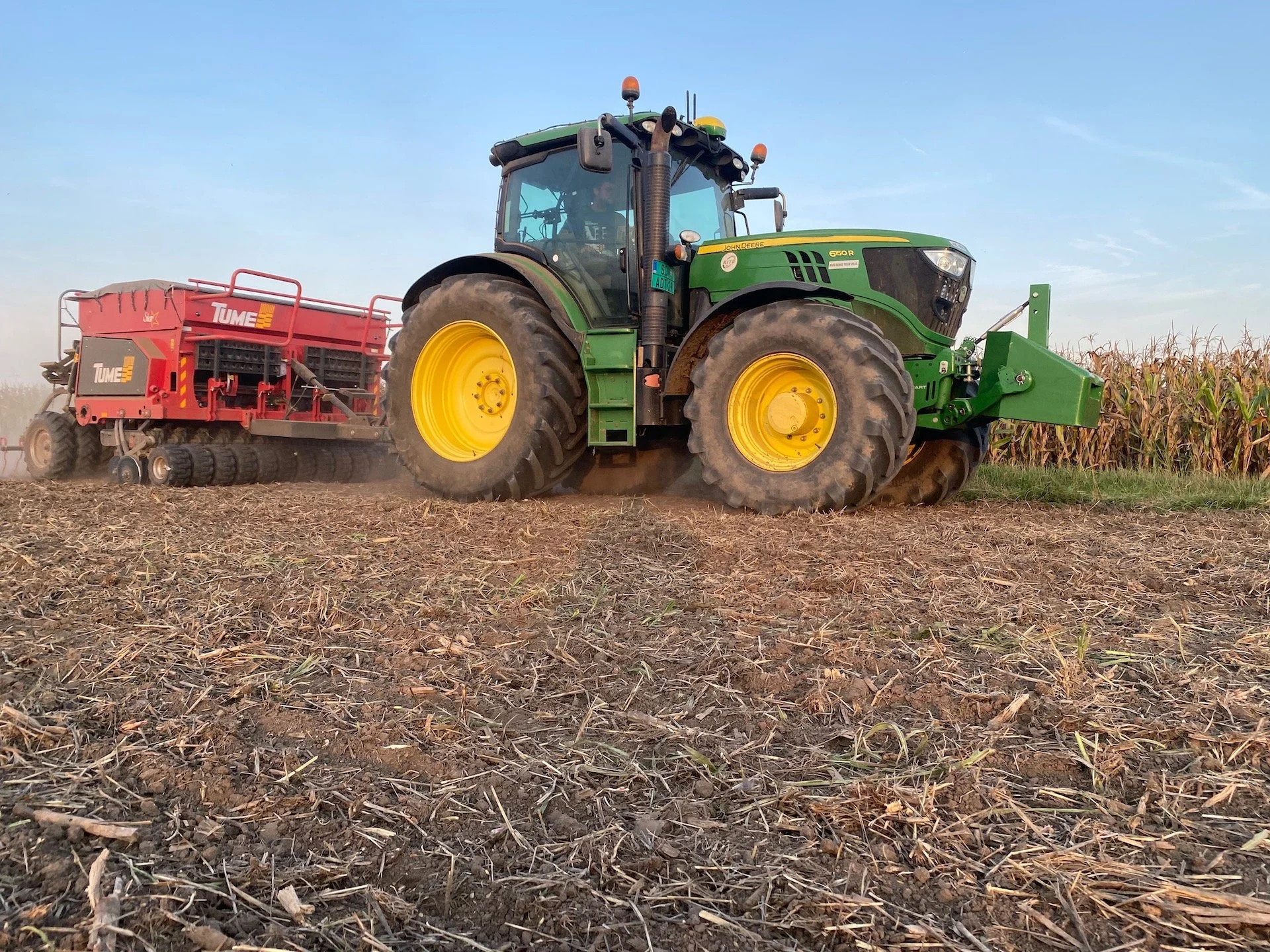 Veliki zeleni traktor sa crvenom sejalicom radi na polju posle žetve.