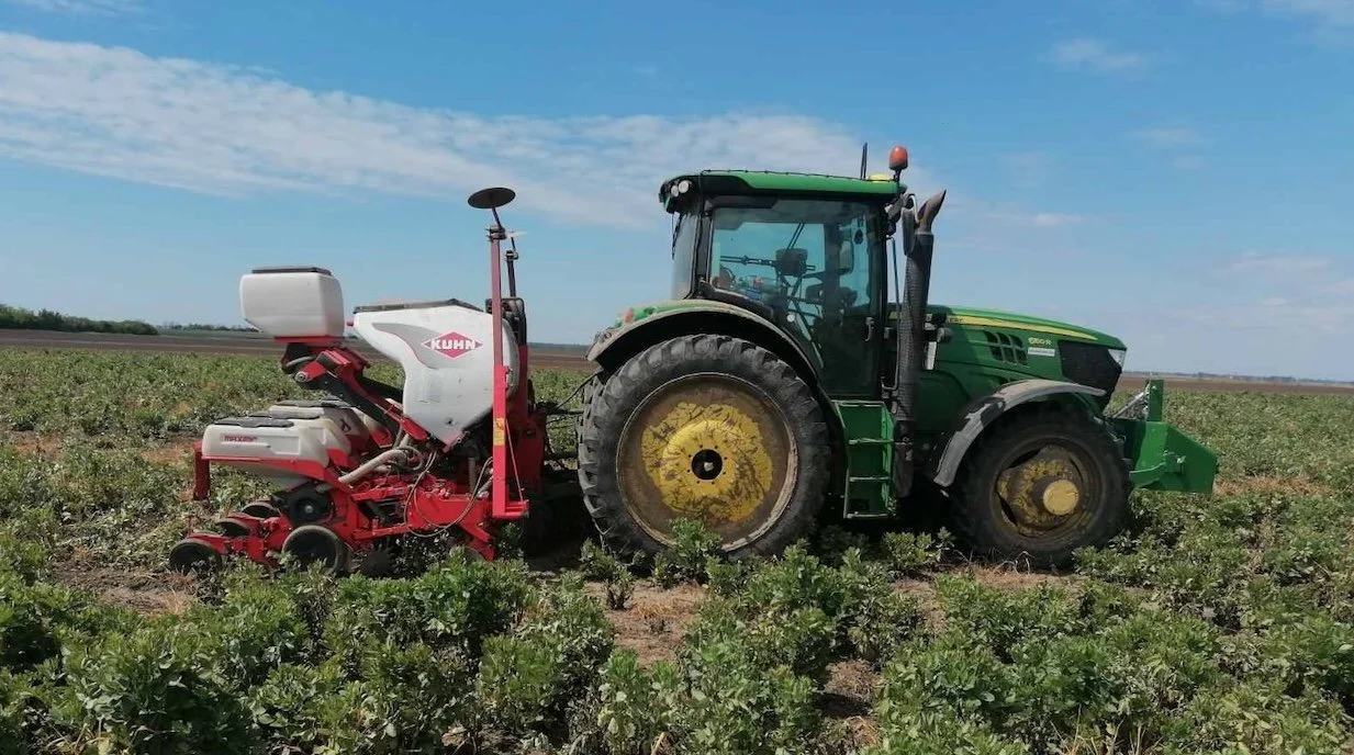 Zeleni traktor sa crvenom sejalicom seje usev na zelenoj njivi.