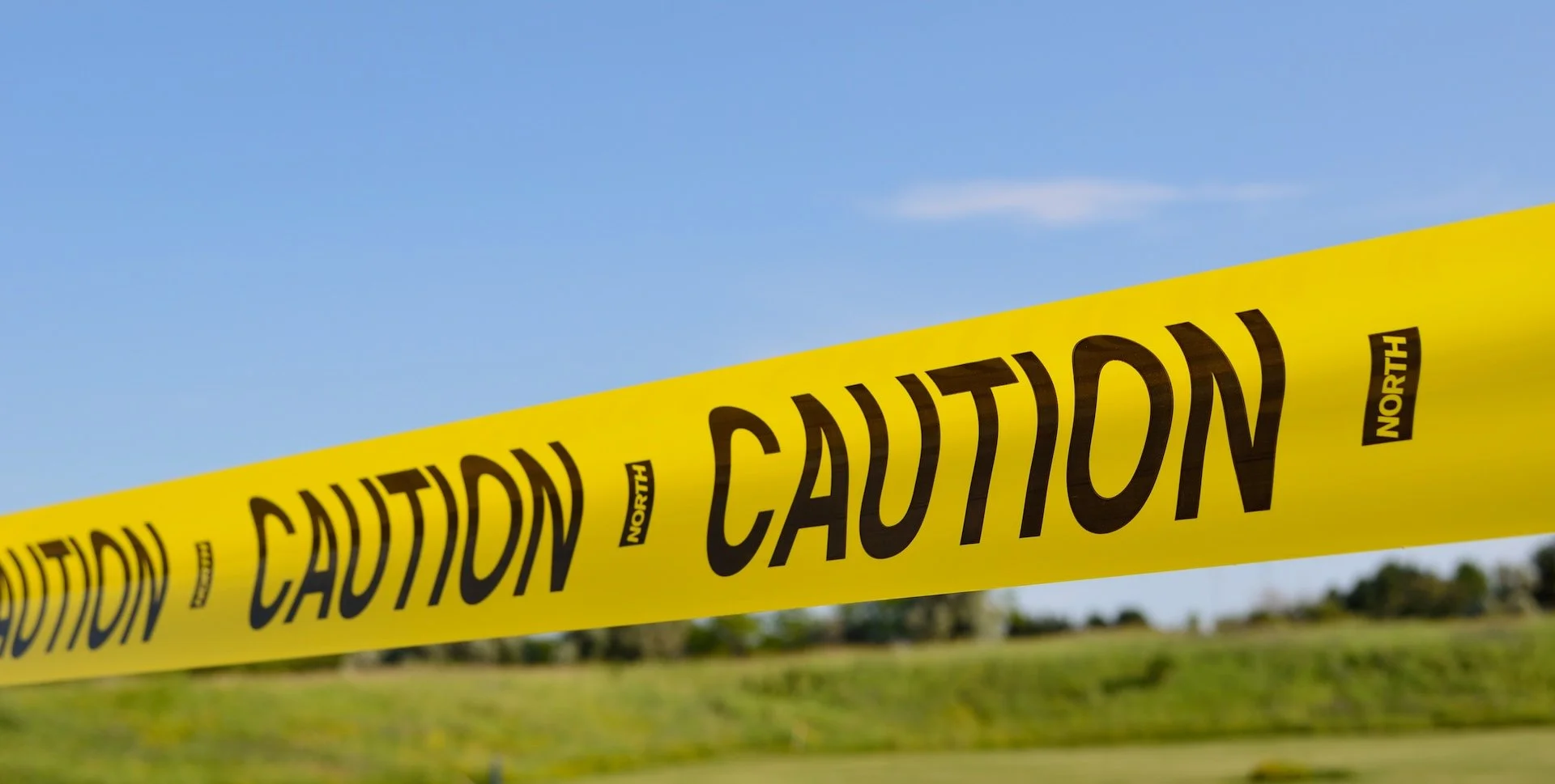 Žuta traka sa crnim natpisom &bdquo;CAUTION&rdquo; na zamućenoj pozadini.